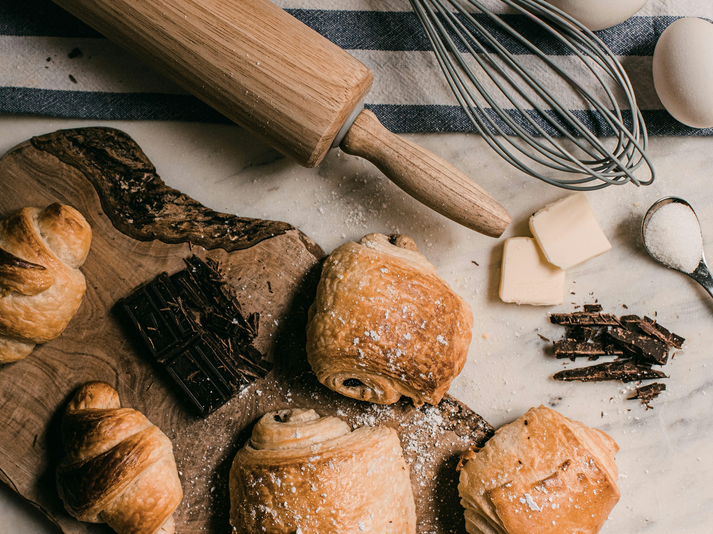 Croissants, pain au chocolat, chocolate and butter on a wood board with linen and a rolling pin